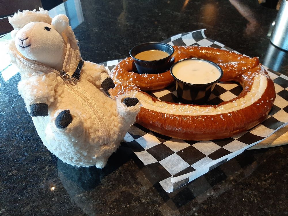 the sheep plushie sitting next to a large baked pretzel