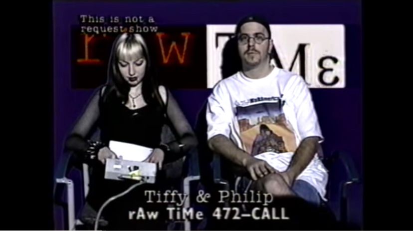 Screenshot of two peopl sitting in chairs in front of a bad green screened background and the word Raw Time behind them