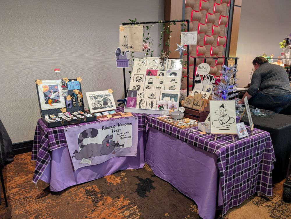 market/artist table set into an L shape. there's a bunch of purple and lino prints. 