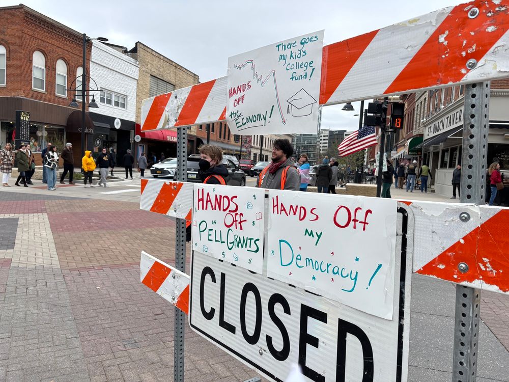A traffic barricade with signs reading "Hands off the economy" "there goes my kid's college fund" "hands off Pell grants" and "Hands off my democracy"