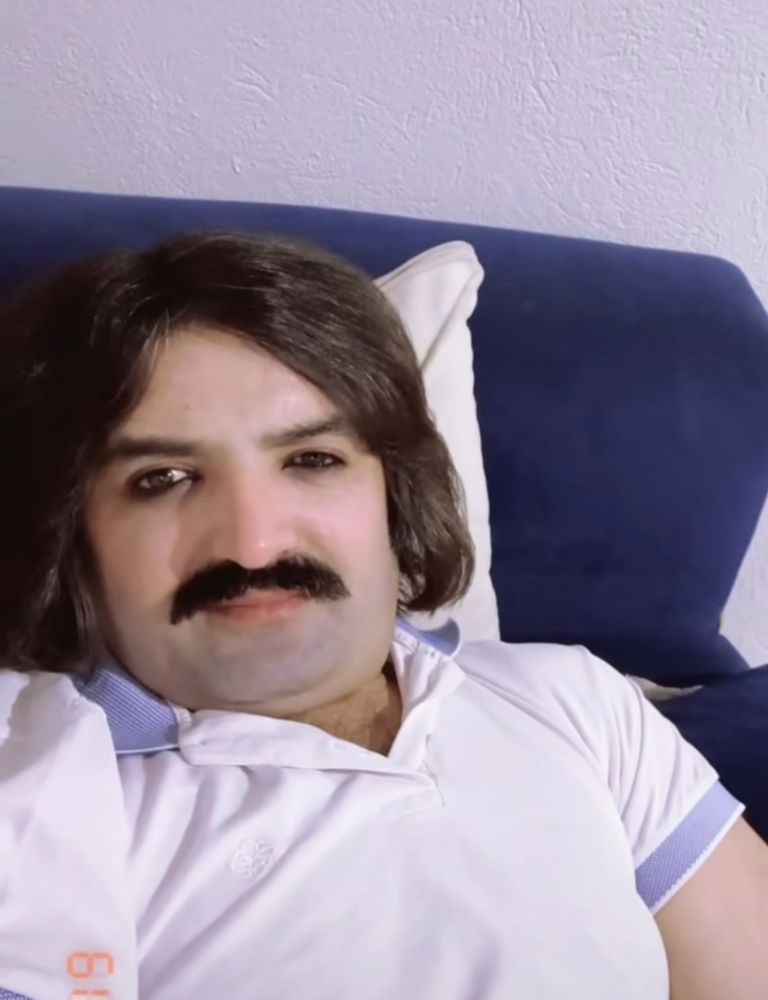 Homem branco com cabelo de playmobil e bigodes grossos, camisa polo e olhar penetrante para camera