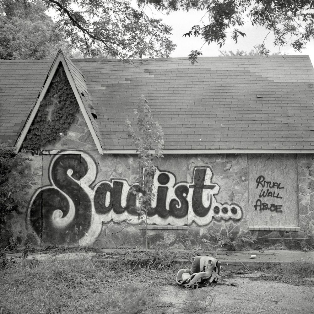 A black and white film photo. An abandoned house has a large graffiti tag that reads “Sadist… Ritual Wall Abuse” in Austin, Texas. Monday, June 23, 2025. 