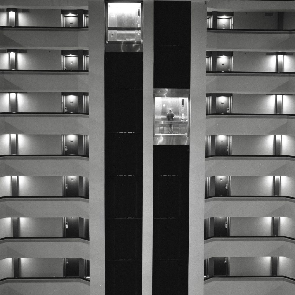 A black and white film photo. A wide shot of a solitary figure riding an elevator in Houston Texas. Thursday, November 23, 2023.