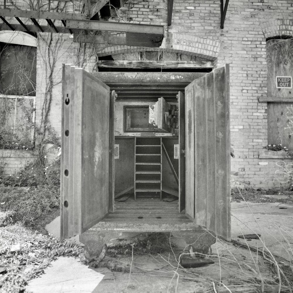 A black and white film photo. A large antique metal safe sits open outside an abandoned building in Smithville, Texas. Saturday, March 22, 2025.