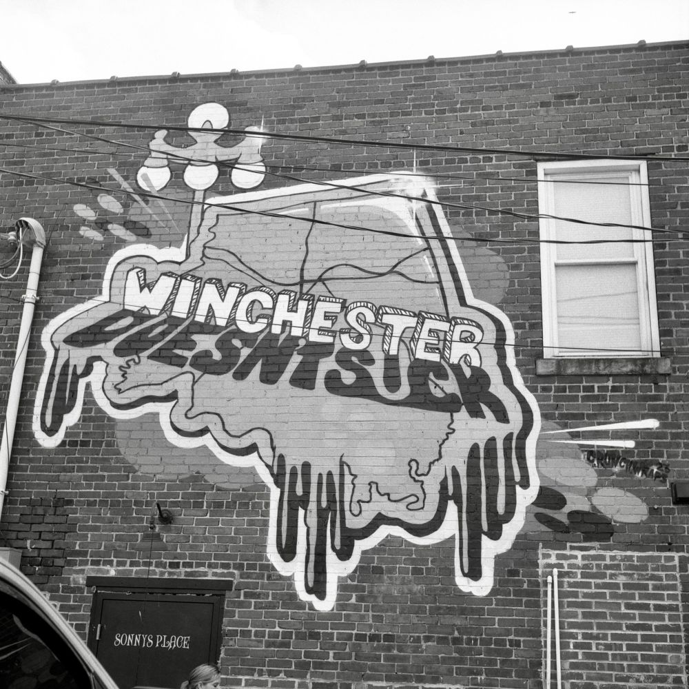 A black and white film photo. Graffiti on an old building’s brick wall states that “Winchester Doesn’t Suck” in Winchester, Kentucky. Friday, July 18, 2025.