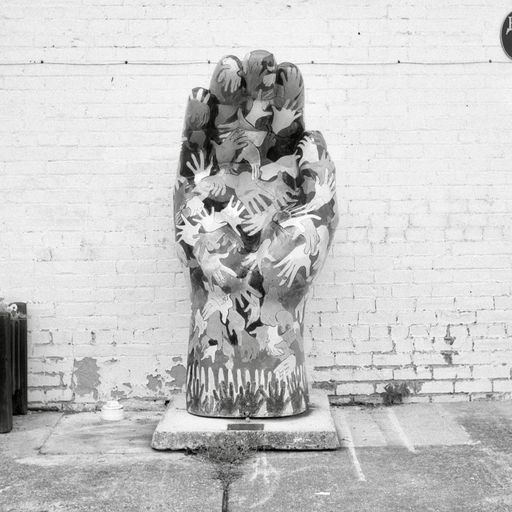 A black and white film photo. A street art installation of large hand sculpture is covered with depictions of hands in Berea, Kentucky. Friday, July 18, 2025.