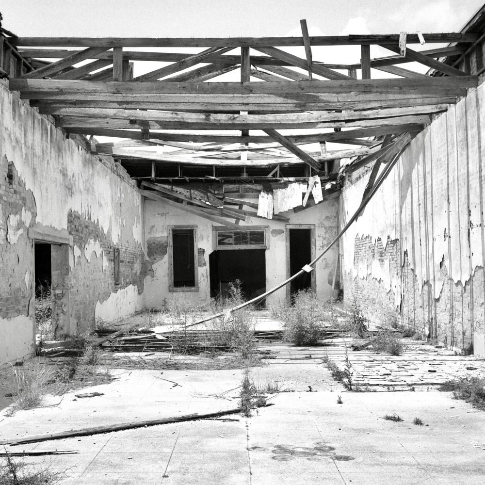 A black and white film photo. Only the wood rafters remain from the roof of an old abandoned building in Bartlett, Texas. Sunday, June 15, 2025.