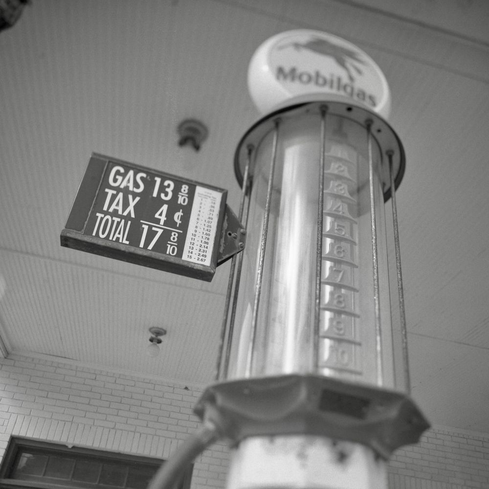 A black and white film photo. An antique gas pump displays the cost of gas, which was 17 8/10 cents per gallon, at a very old gas station in Smithville, Texas. Sunday, June 29, 2025.