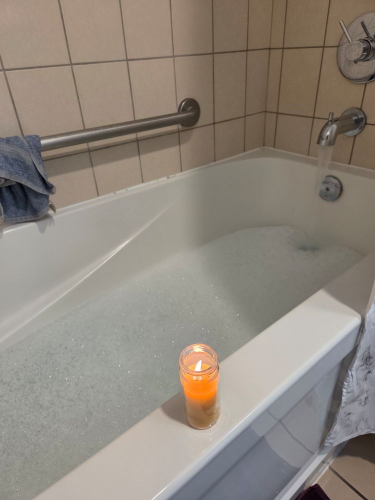 Bathtub filling with bubbles. Tiny yellow candle perched on the edge of the white tub.