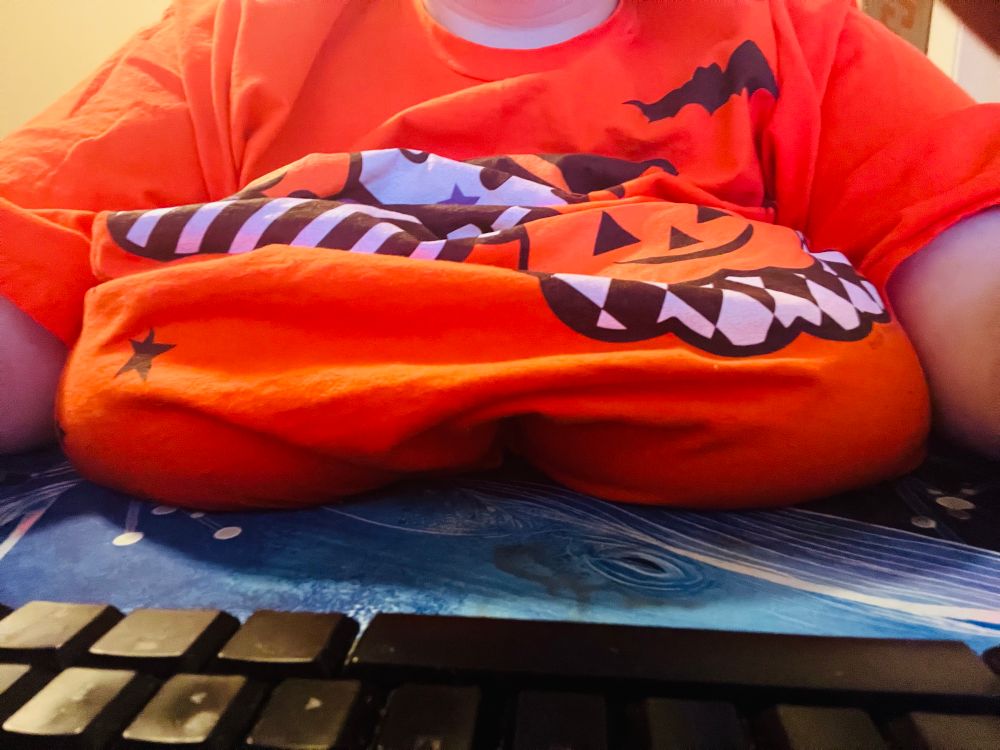 Hex sitting at their desk with the clothed tits on their desk. 