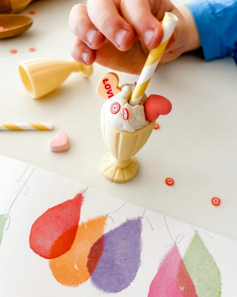 The picture book “Happy All Over”, open to a colourful illustration by Emma Quay and with ice-cream sundae toys and confetti scattered around.