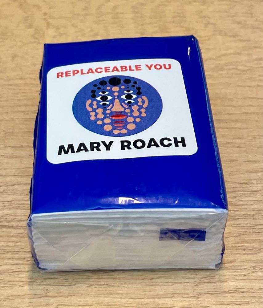 A small packet of tissues, with a sticker on it saying “Replaceable You” and “Mary Roach” with the art from the book cover — a face made up of multiple disconnected features (six eyes, three mouths, blobs of skin and hair)