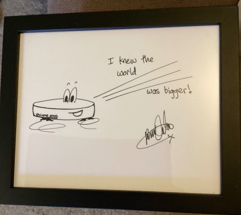 Framed print of some amazing Rhys Darby art of a Roomba with eyes and looking kinda cute! Also has his signature and the words “I knew the world was bigger!”