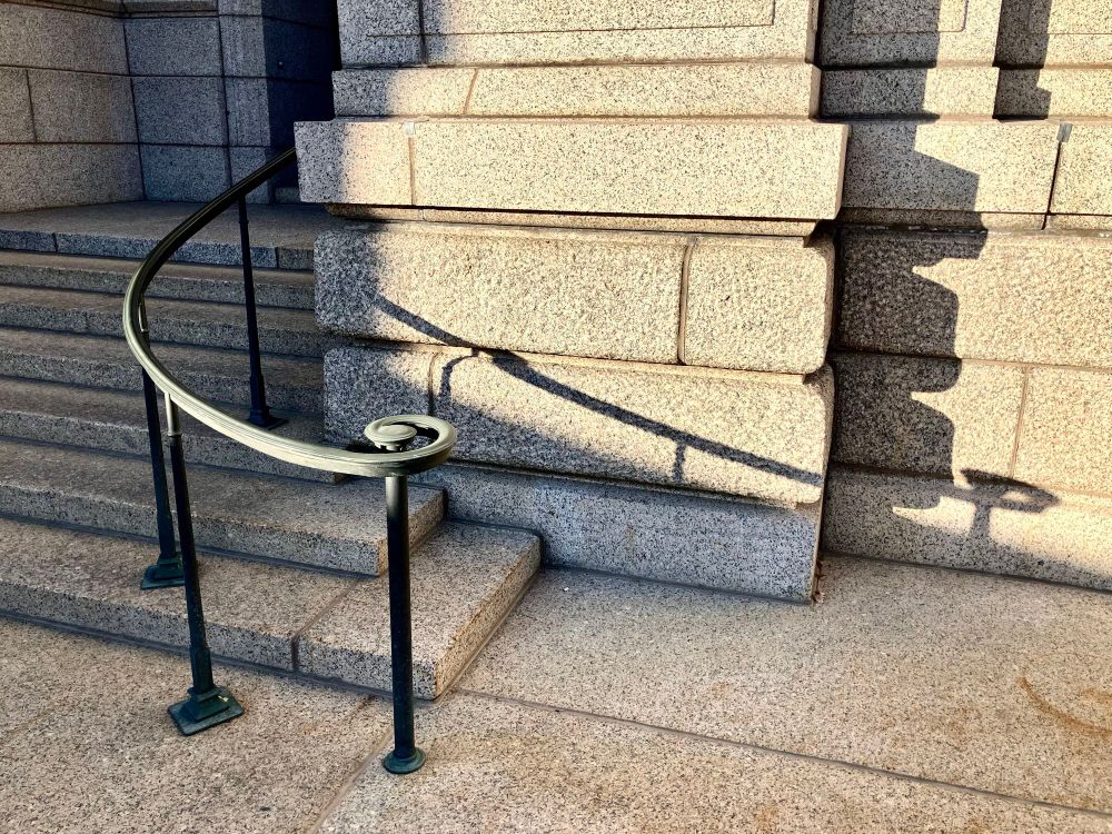 curved ornamental metal hand rail down stone stairway in late day sunlight with long shadow