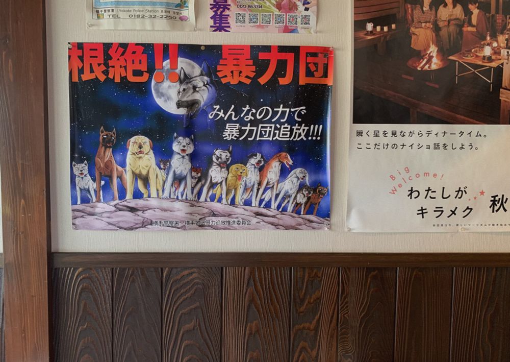 壁に貼られた暴力団追放ポスター。『銀牙』に登場する犬たちが並んだイラスト。「根絶！！暴力団」「みんなの力で暴力団追放！！！」という文字が書かれている。
