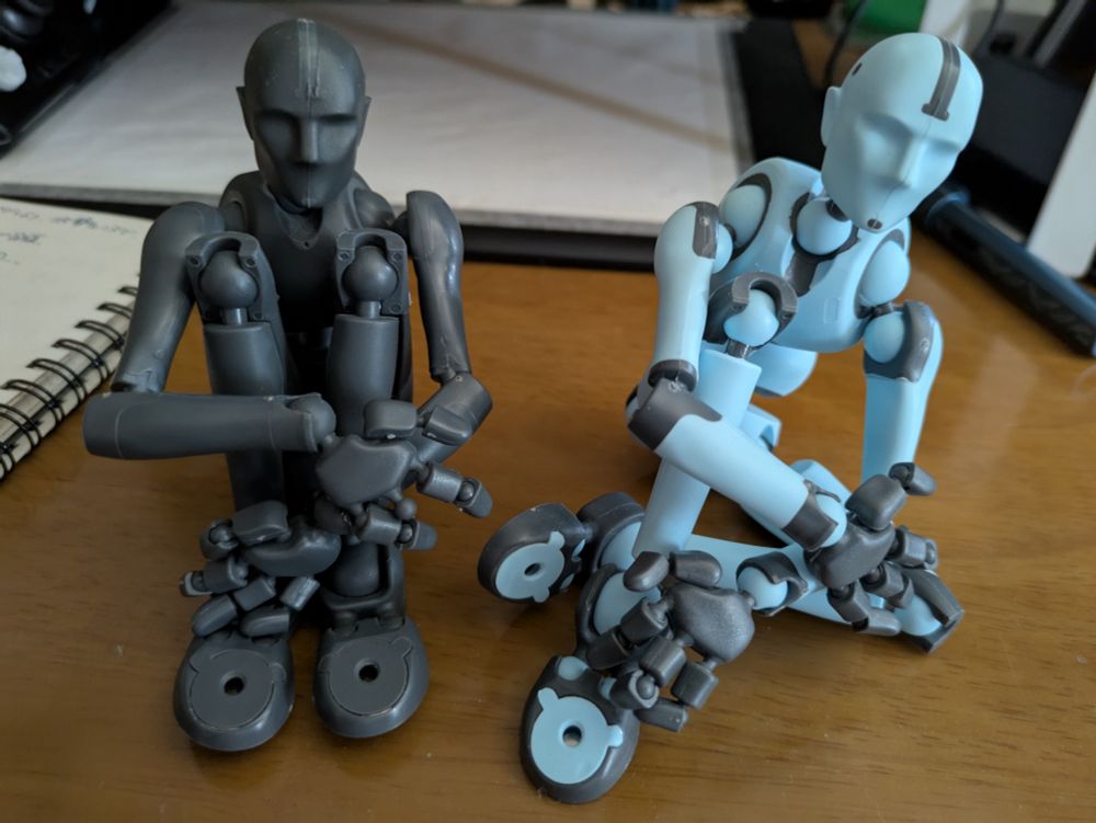 無機質なデッサン人形2体。左は両ひざを抱え体育座りしている黒いデッサン人形。右は片ひざを抱えゆるく座る水色のデッサン人形。どちらもスティッキーボーンズというポーズ人形。