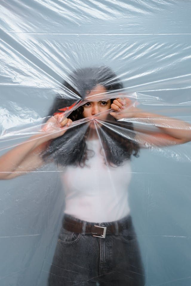 Woman looking empowered, tearing open translucent plastic that has been keeping her from full view Image by Mart Productions Pexels