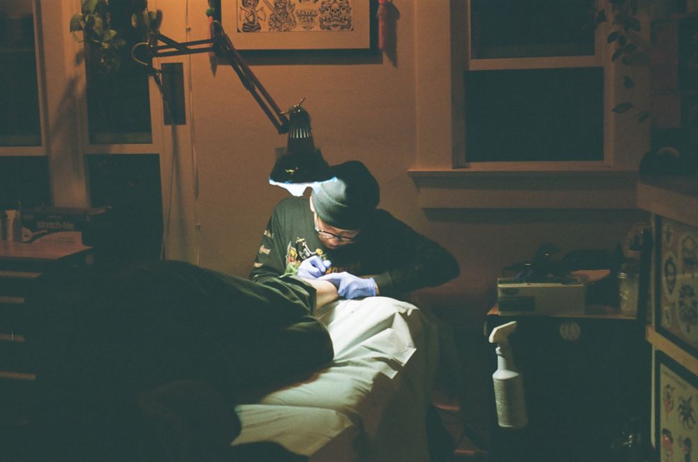 film photo of a tattooer working under a spotlight.
