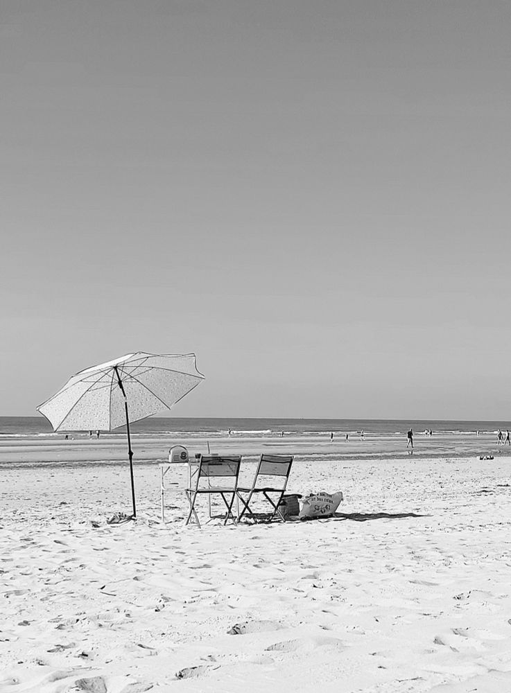 Noir et blanc d'un bord de plage avec un parasol ouvert sur la gauche accompagné de 2 chaises désertées au centre