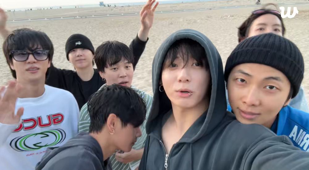 bts ot7 at the beach in LA on weverse live today. namkook are at the front of the frame, jungkook holding the camera while namjoon rests his chin on jungkook's shoulder.