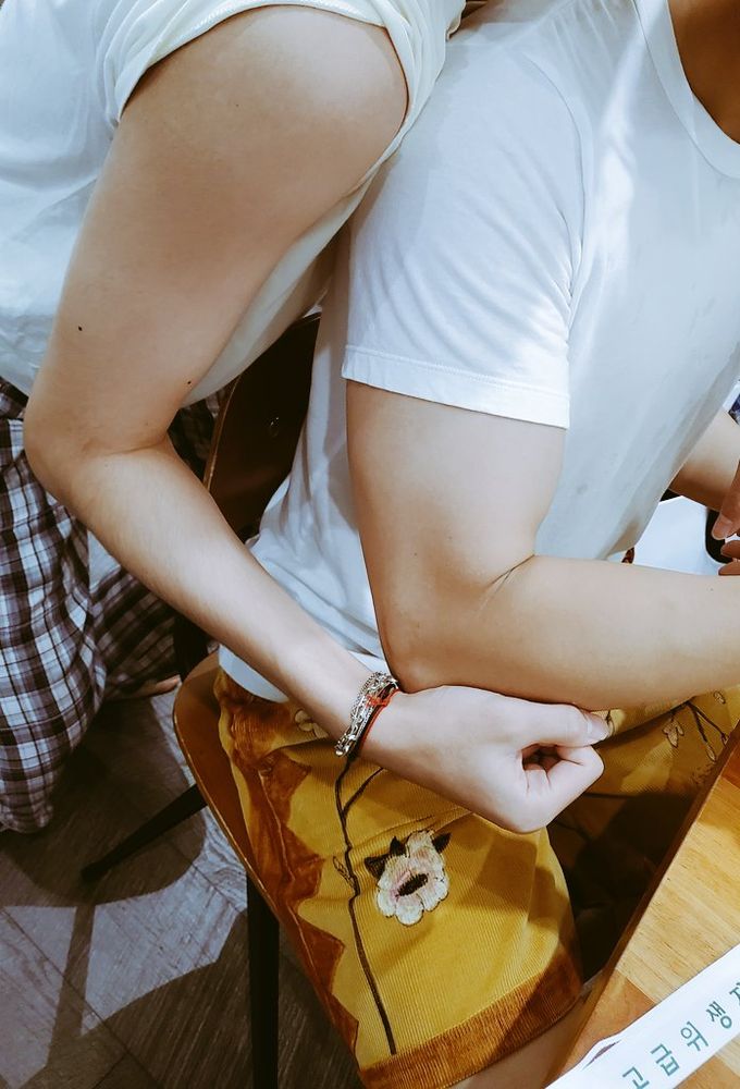 taehyung with his sleeve rolled up, namjoon seated in a white tee in front of him. taehyung is flexing his arm just behind namjoon's to compare their muscles. namjoon's biceps look huge, and taehyung is much skinnier in comparison. their faces are cropped out of the photo, which gives the whole thing a distinct thirst trap energy.