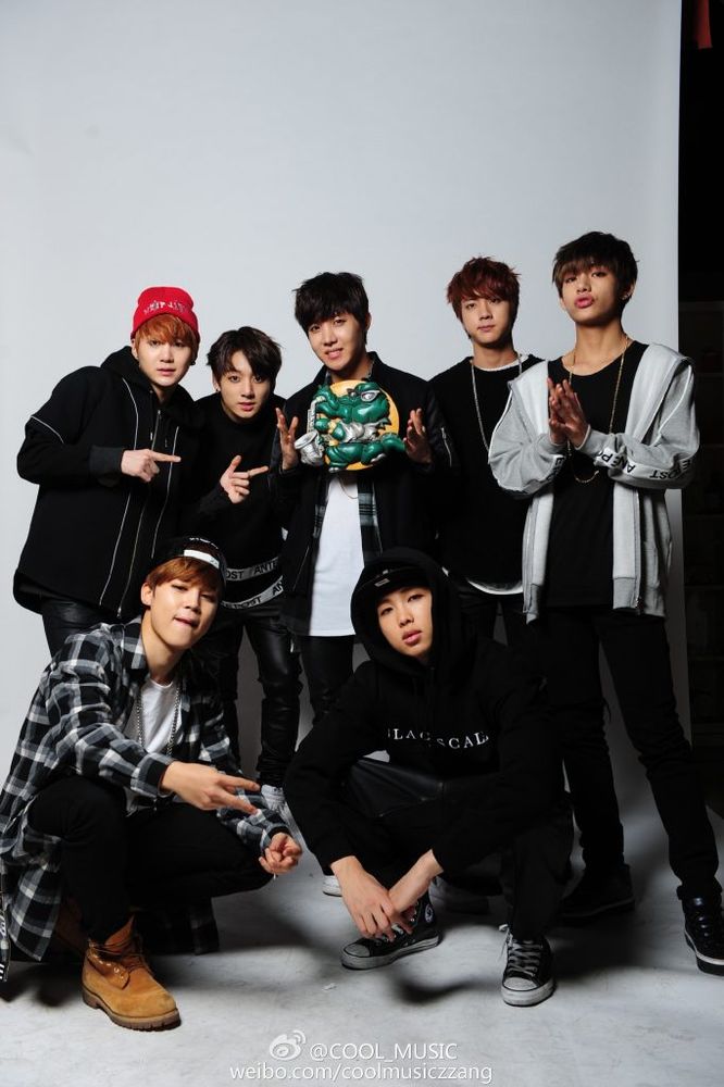 bts ot7 in a 2015 photoshoot for cool music magazine. they're dressed in black and gray streetwear with namjoon and jimin crouched in front, posing like they're hard. in the back, hobi in the center is displaying a round yellow disc with a logo of a sunglasses-wearing alligator playing the sax. yoongi and jungkook are helpfully pointing at it.