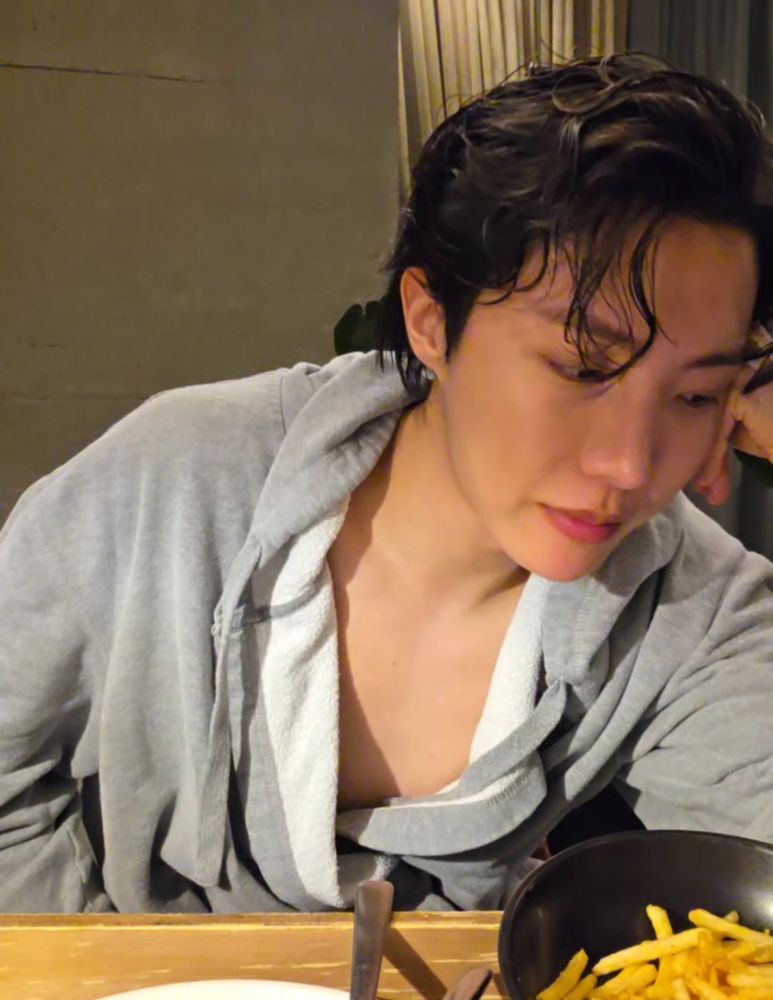 j-hope on weverse live in a loose bathrobe, leaning his head on his hand and looking down.