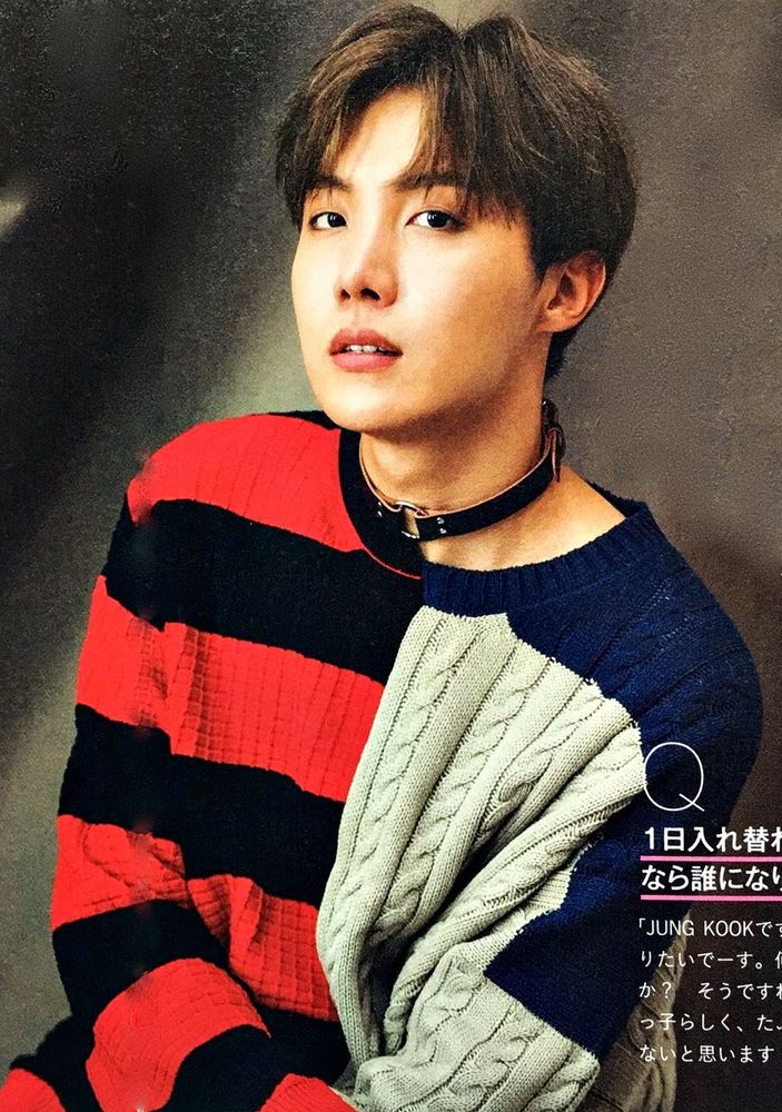 hobi in a sweater split down the middle - half red and black horizontal stripes, half grey chunky knit with navy blue shoulders. he's wearing a brown leather buckled choker with an o ring in the front, and he's gazing up into the camera with his mouth slightly slack. it makes his neck look great.