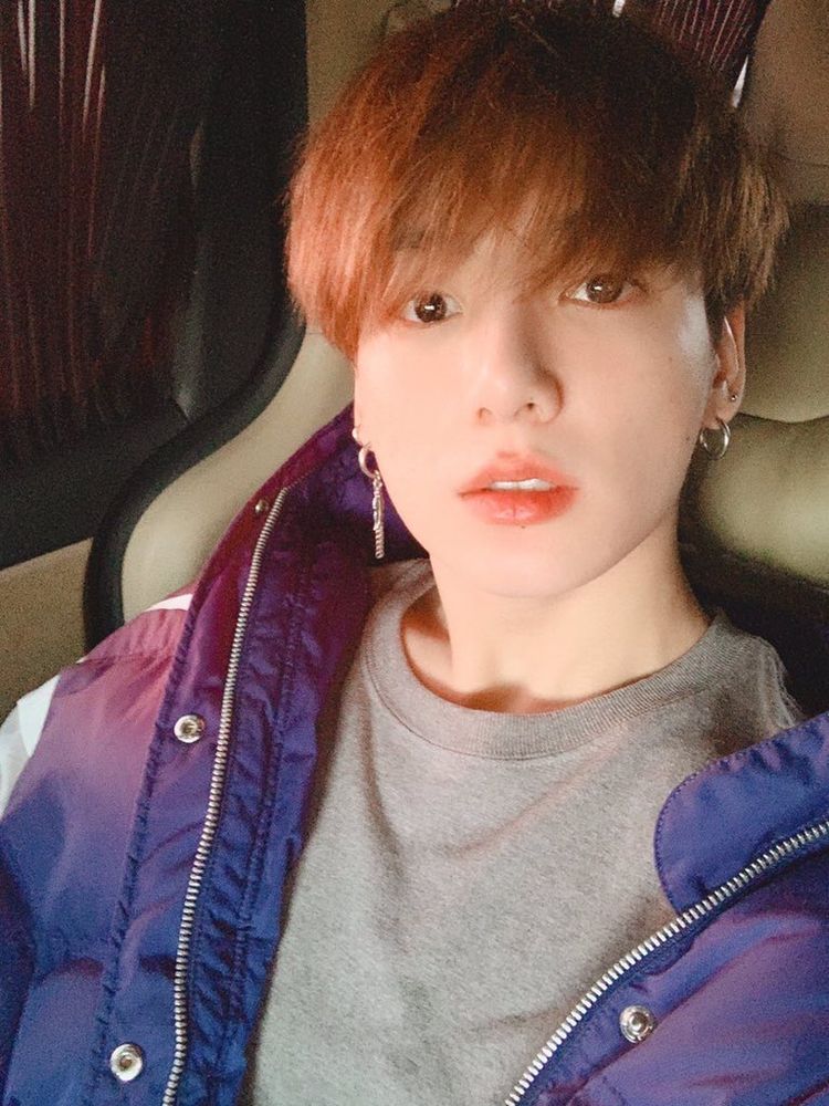 jungkook in a car with drawn privacy curtains, wearing a puffer jacket and one dangly earring. his lips are parted and his mouth looks more swollen than usual and his bangs are partly falling into his eyes.
