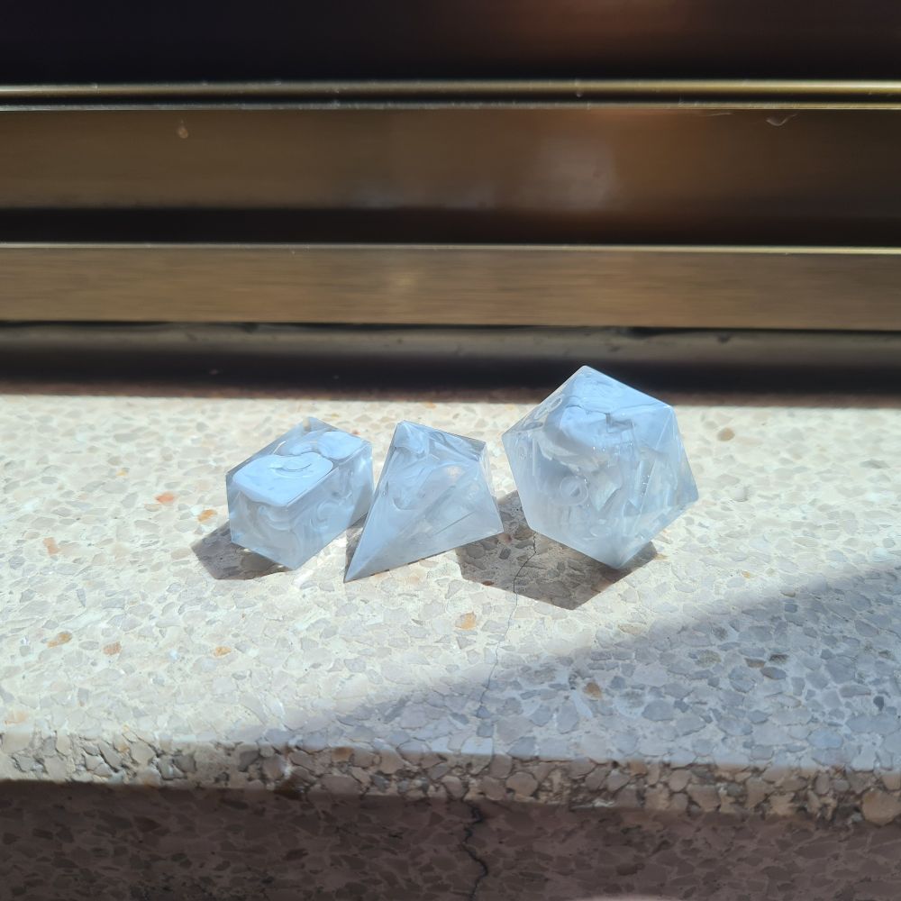 One d20 and two d4s on a flat surface. They are transparent with smoke-like grey swirls.