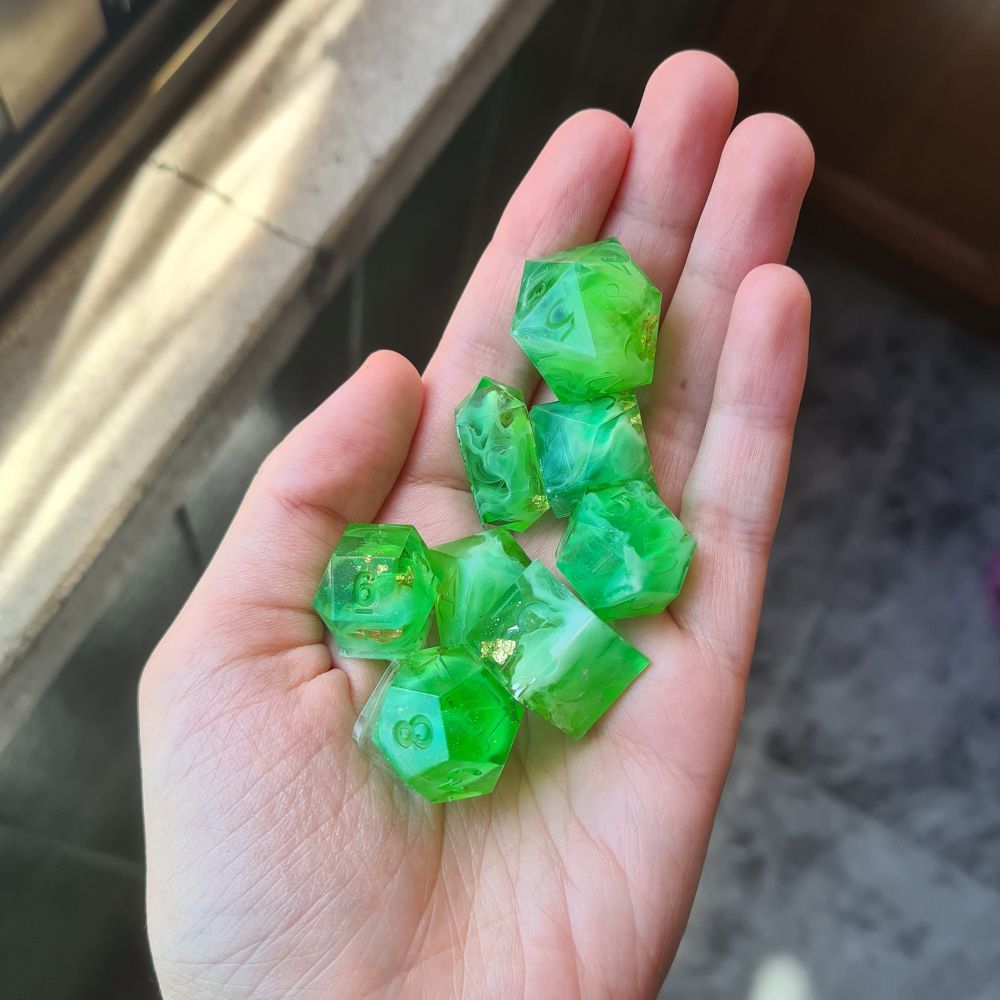 Set of 8 dice with various shapes on my hand. They are green with white swirls and a few pieces of gold leafs.
