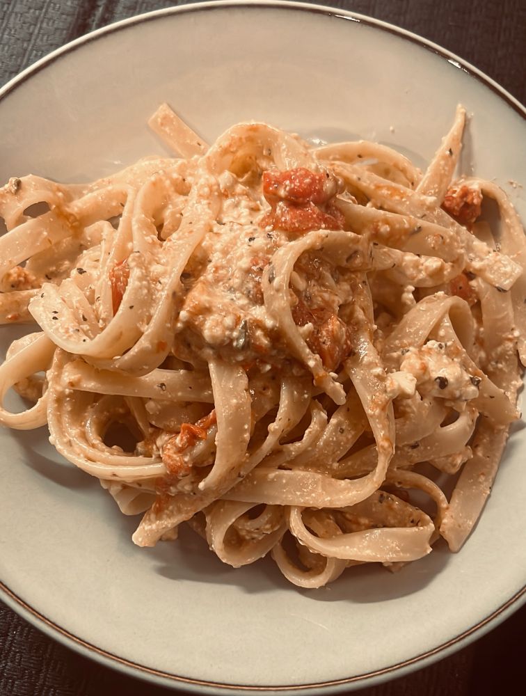 A plate of fettuccine with baked feta and cherry tomato sauce. 