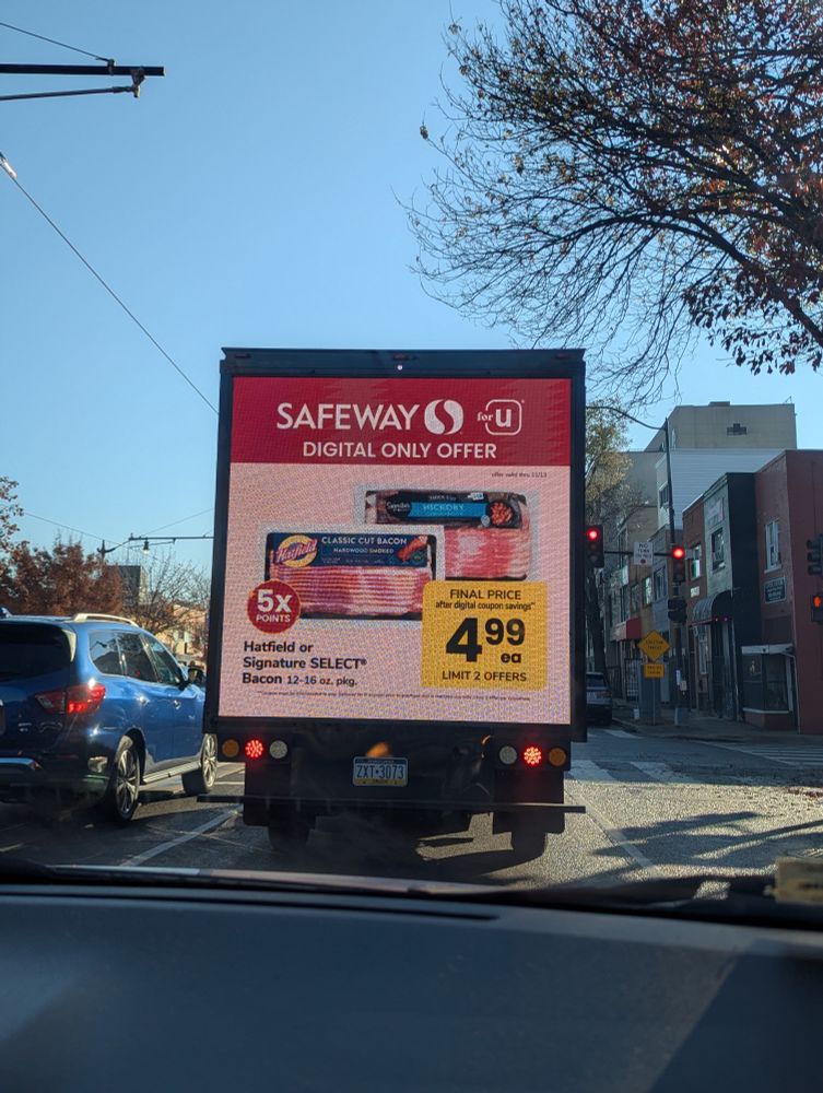 A digital billboard on the back of a grocery delivery truck advertising bacon 