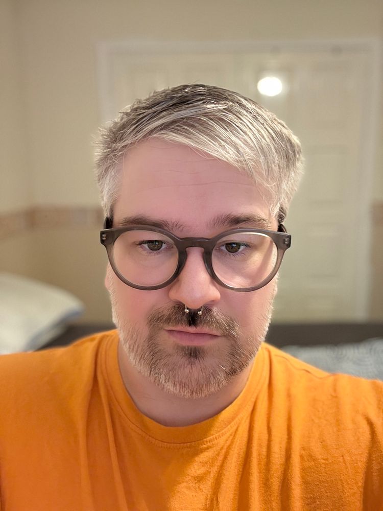 A selfie of me. Wearing grey/brown glasses and an orange t-shirt
