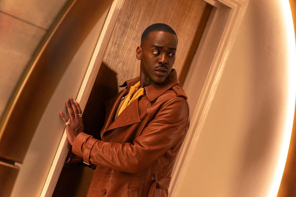 Ncuti Gatwa as the Fifteenth Doctor,
from the Christmas Special JOY TO THE
WORLD. He has a hand leaned on the wall and is looking at something behind him