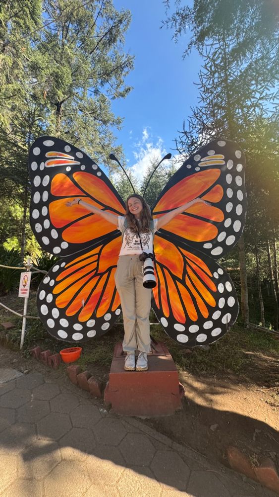 Rachael standing with a giant butterfly wing cutout 
