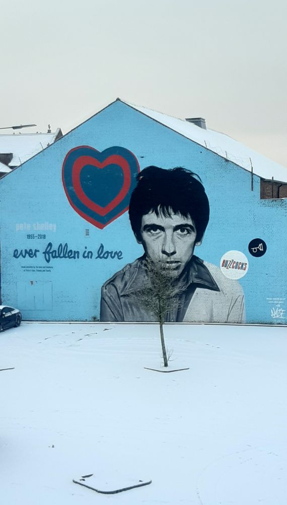 Mural of Pete Shelley (Buzzcocks) in Leigh with snow in foreground and white cloudy sky
