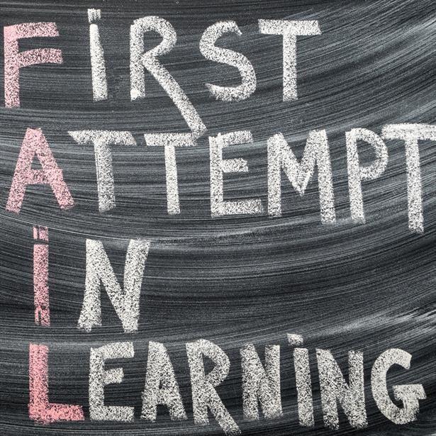 Color image: a recently erased chalkboard with the words "First Attempt In Learning" written in large white letters, one word per line. The first letter of every word is pink. Reading from top to bottom, the pink letters spell the word 'FAIL'.