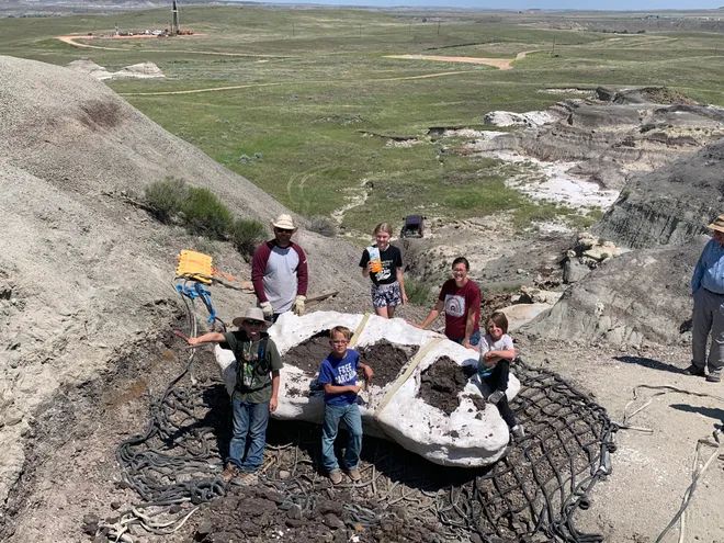 "Sam Fisher, his sons Jessin and Liam, their cousin, Kaiden Madsen, and paleontologist Tyler Lyson unearthed a teenage T. rex fossil in the summer of 2023 in North Dakota."

Image is a photograph of the above-named group surrounding their fossil find, taken from above.