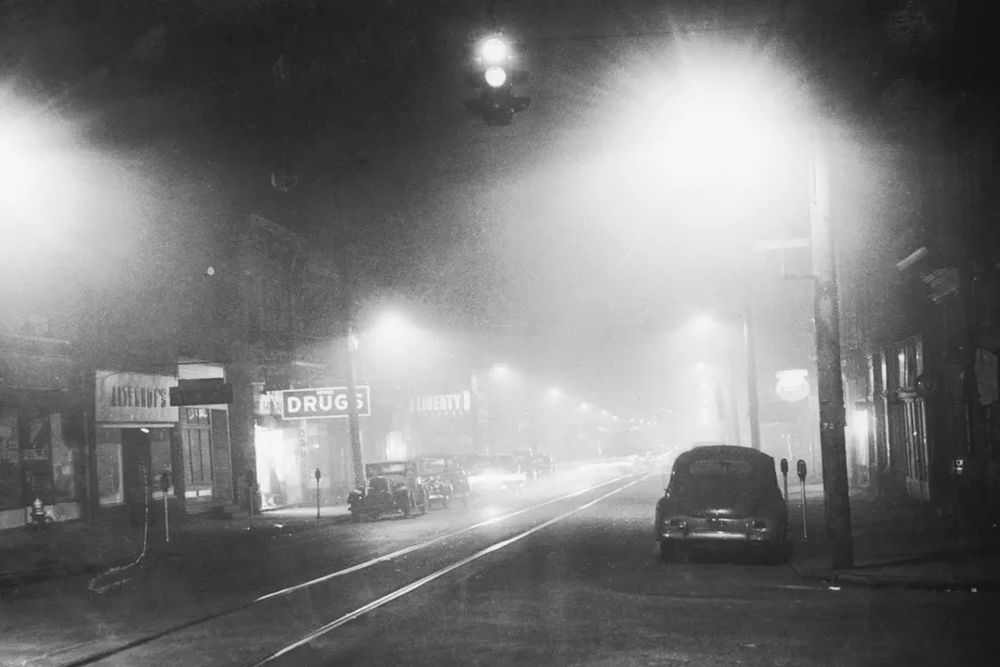Black-and-white photo: image of a car parked at the curb of a smoggy downtown street in Donora PA. The photo, taken at noon, looks as though it were taken in the dead of night.

📸: Bettman