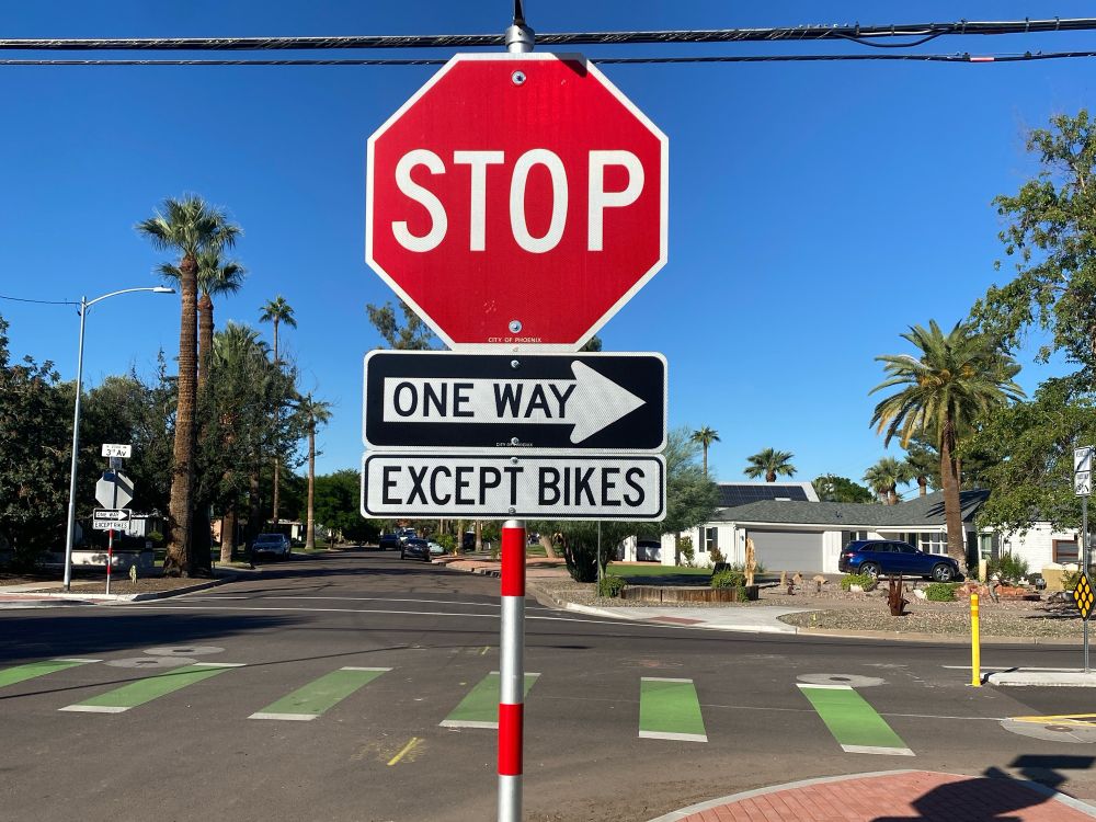 A photo of a stop sign. Underneath, it says "One Way" and underneath that it says "Except Bikes"