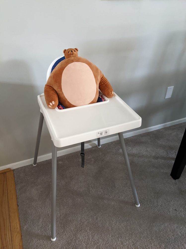 A large plush bear with a small head sitting in a baby’s high chair