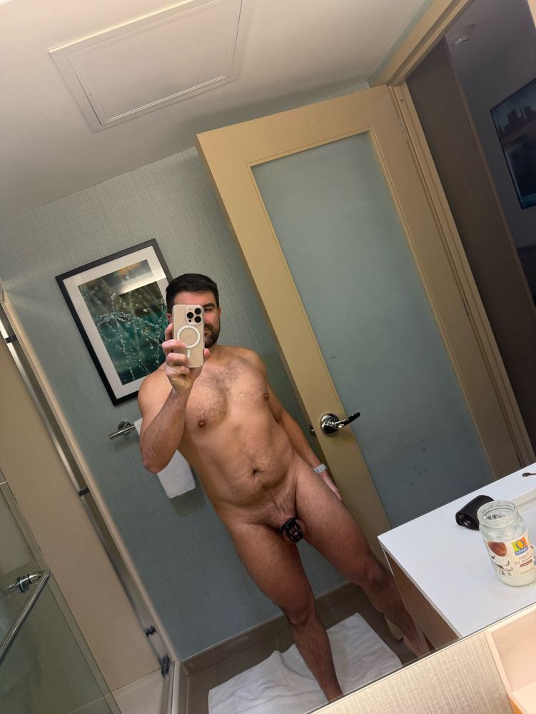 Naked guy in a hotel room wearing a chastity cage. 