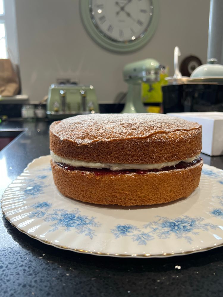 Homemade Victoria sponge cake with jam and buttercream filling on a china plate decorated with blue flowers. 