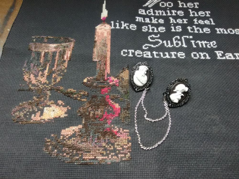 progress picture of a cross stitch project, showing a candlestick with lit candle, a crystal goblet, and reflections from a red rose, yet to be stitched