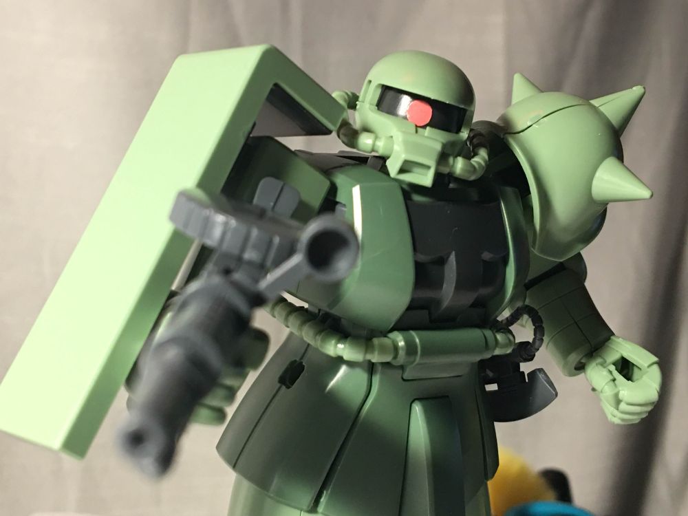 assembled model kit of a green zaku from gundam, close-up of the face and chest area, gun is pointing towards the camera