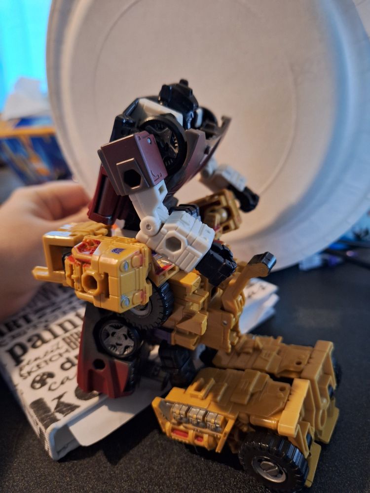Swindle on his knees, one arm wrapped around sideswipe's aft, positioned to look like he's sucking sideswipe's spike
Sideswipe is propped up on a book, one arm resting on swindle's back