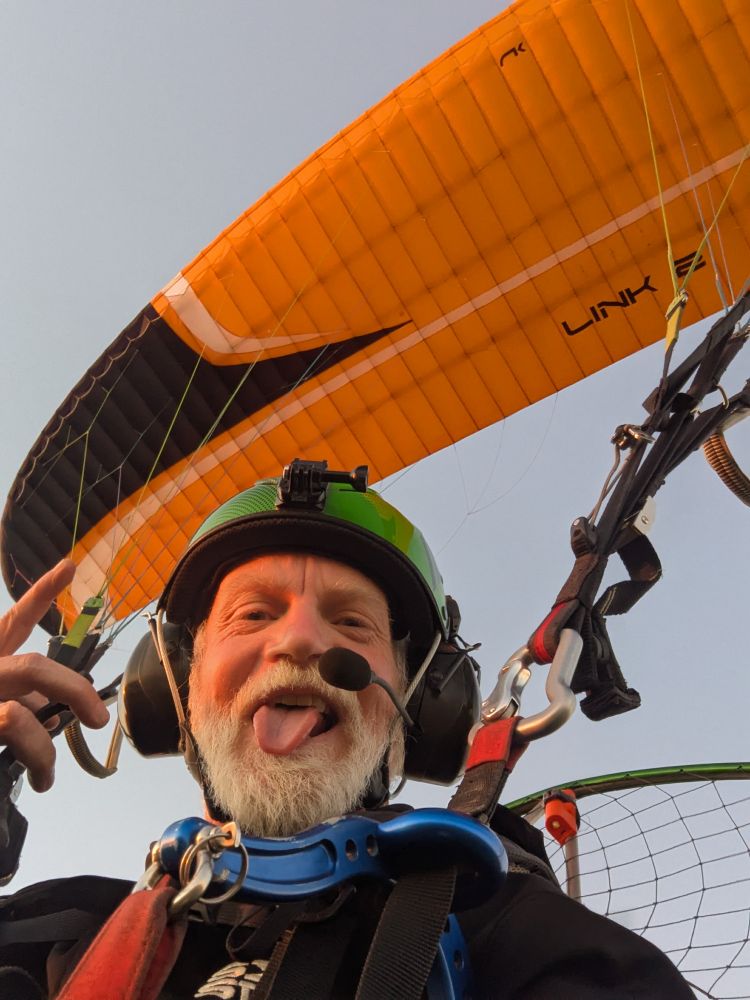 Selfie while flying my paramotor. I've got the camera in my lap, pointing toward the glider, and sticking my tongue out in the photo.