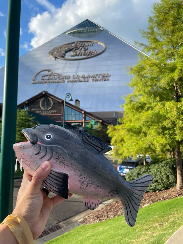 holding up my singular purchase in front of the bass pro pyramid. its a wooden catfish 