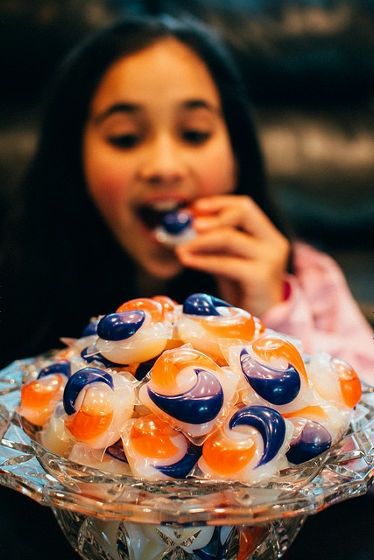 A candy bowl full of tide pods with an out of focus girl in the background eating one